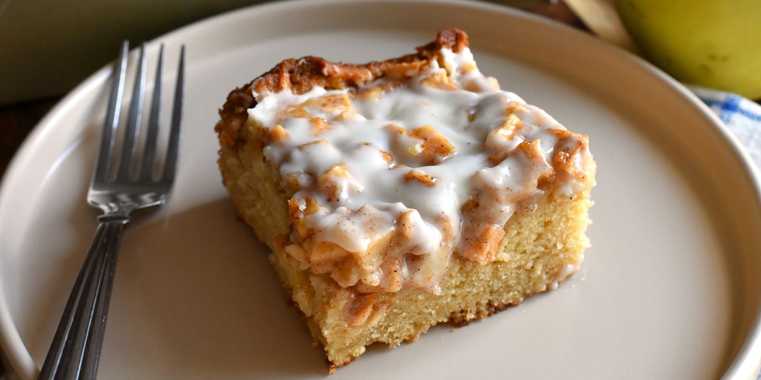 Apple fritter cake topped with vanilla icing, placed on a decorative plate, showcasing its warm cinnamon color and apple chunks.